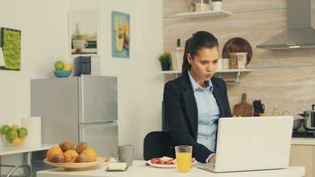 affaires femme en mangeant grillé pain avec beurre tandis que travail sur portable pendant petit déjeuner. concentré affaires femme dans le Matin multitâche dans le cuisine avant Aller à le bureau, stressant façon de vie, carrière et buts à rencontrer photo