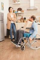 invalide homme dans fauteuil roulant avec les courses sac ayant une conversation avec épouse dans cuisine. désactivée paralysé handicapé homme avec en marchant invalidité en intégrant après un accident. photo