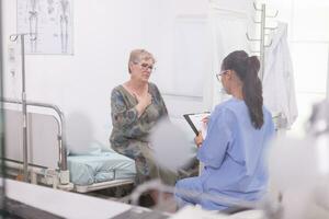 Sénior patient discuter à propos maladies avec infirmière pendant médical examen dans hôpital bureau. photo