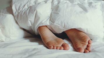 enfant pieds nus en dessous de blanc duveteux couverture. enfant cache pieds en dessous de chaud coton couverture. sommeil et relaxation dans hôtel, paresseux Matin pour les enfants. réveiller en haut avoir prêt pour école. photo