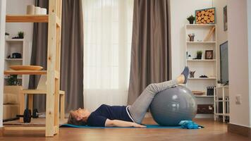 Sénior femme formation aptitude Balle mensonge sur yoga tapis dans vivant chambre. vieux la personne en bonne santé mode de vie retraité vivant sport et bien-être formation à l'intérieur à Accueil photo