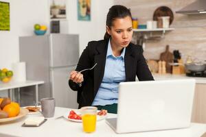 homme d'affaires en mangeant petit déjeuner tandis que travail de maison. concentré affaires femme dans le Matin multitâche dans le cuisine avant Aller à le bureau, stressant façon de vie, carrière et buts à rencontrer. photo