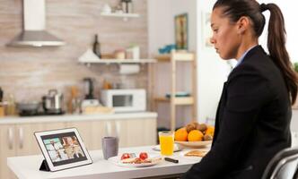 femme parlant avec collègues sur vidéo came à propos le suivant projet. Jeune pigiste dans le cuisine parlant sur une vidéo appel avec sa collègues de le bureau, en utilisant moderne l'Internet La technologie photo