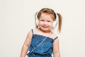 mignonne peu fille dans écouteurs écoute à la musique en utilisant une tablette et souriant sur blanc Contexte photo