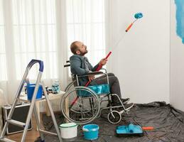 invalide homme La peinture mur tandis que séance dans fauteuil roulant. handicapé, désactivée mauvais et immobilise homme portion avec appartement redécoration et Accueil construction tandis que rénover et améliorer, photo