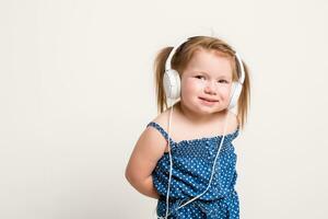 mignonne peu fille dans écouteurs écoute à la musique en utilisant une tablette et souriant sur blanc Contexte photo