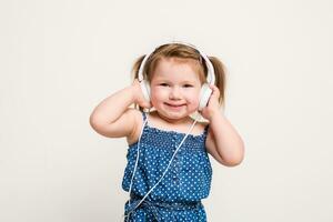 mignonne peu fille dans écouteurs écoute à la musique en utilisant une tablette et souriant sur blanc Contexte photo