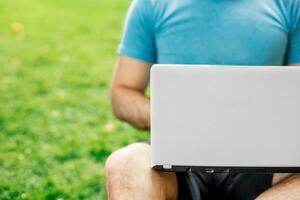 Jeune homme en utilisant et dactylographie portable ordinateur dans été herbe. photo