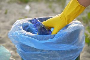 Jeune bénévole dans Jaune gants est en marchant avec des ordures sac le long de une sale plage de le rivière et nettoyage en haut poubelle. gens et écologie. fermer. photo