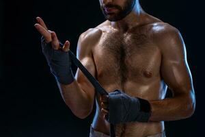 boxeur en train de préparer sa gants pour une lutte. photo de musclé homme cerclage en haut mains sur noir Contexte.