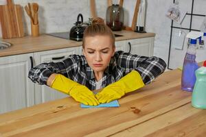 Jeune femme dans protecteur gants lingettes une table dans le cuisine avec une chiffon photo