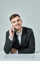 Beau Jeune homme parlant sur le mobile téléphone tandis que séance à le sien travail endroit dans Bureau photo