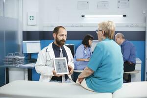 pendant médical vérification, soins de santé spécialiste spectacles image de Humain squelette sur tablette à personnes âgées patient. Masculin médecin détient en haut gadget cette affiche examen de des os et diagnostics ostéopathie. photo