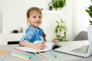 mignonne peu fille est séance à table avec sa portable et en train d'étudier en ligne photo