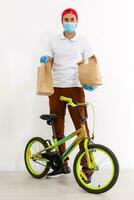 une homme dans protecteur masque est livrer nourriture sur une vélo. en ligne achats et Express livraison . quarantaine photo