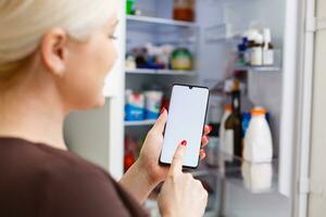 fermer de femme main en utilisant énergie étiquette sur mobile téléphone contre réfrigérateur à Accueil photo
