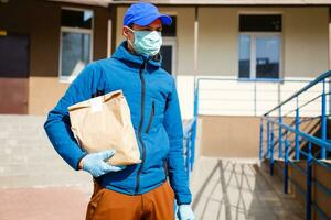 livraison homme en portant papier sac avec nourriture, nourriture livraison homme dans protecteur masque photo