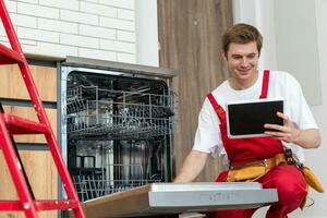 portrait de Masculin technicien réparer Lave-vaisselle dans cuisine en utilisant numérique tablette. photo