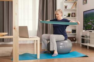 60 ans vieux femme exercice de maison. vieux la personne retraité en ligne l'Internet exercice formation à Accueil sport activité avec haltère, la résistance groupe, Suisse Balle à personnes âgées retraite âge photo