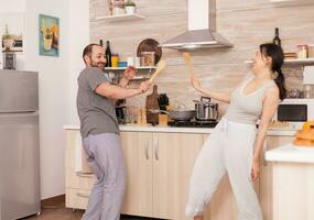 marrant couple dansant dans cuisine pendant petit déjeuner portant pyjamas. insouciant épouse et mari en riant ayant amusement marrant profiter la vie authentique marié gens positif content relation photo