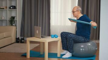 vieux homme sur équilibre Balle formation avec la résistance bande en train de regarder en ligne aptitude programme. vieux la personne retraité en bonne santé formation soins de santé sport à maison, exercice aptitude activité à personnes âgées âge photo