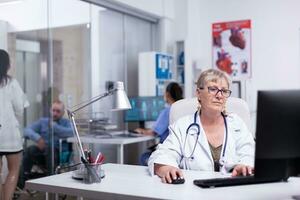 équipe de médecins travail dans hôpital clinique, dactylographie sur ordinateur, infirmière en cours d'analyse corps analyse tandis que Jeune médical discuter avec désactivée furieux dans attendre chambre. expert médecin travail à ordinateur personnel, entrer Les données photo