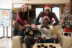 excité collègues équipe dans Père Noël Chapeaux participant dans vidéo jeu compétition dans décoré lieu de travail. de bonne humeur collègues de travail célébrer Noël et en jouant console Jeu ensemble photo