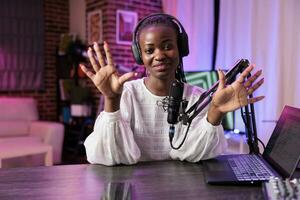 portrait de africain américain l'Internet célébrité diffusion vivre sur diffusion Plate-forme en utilisant professionnel microphone produisant haute qualité sortir. femme création en ligne contenu pour sa Ventilateurs photo