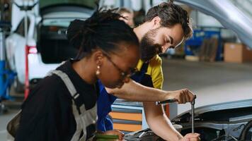 proche en haut coup de cotravail mécanique dans voiture un service en utilisant couple clé à réparer endommagé voiture. homme et africain américain femme dans réparation magasin entretien cassé véhicule en utilisant professionnel outils photo