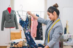 Fille de créateur de mode asiatique faisant la conception de nouveaux vêtements de belle robe bleue avec cintre en studio. showroom élégant de créateur de mode. concept de couture et de tailleur. styliste couturière créative photo