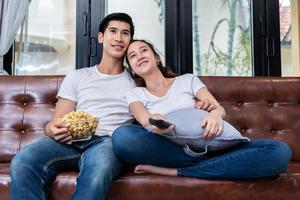 des couples asiatiques regardent la télévision et mangent du pop-corn ensemble sur un canapé dans leur maison. concept de personnes et de modes de vie. thème de la maison et de l'activité heureux