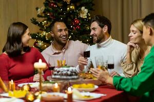 copains célébrer Noël veille ou Nouveau année vacances pâté ensemble séance à le tableau. le banquet à Accueil groupe de multi ethnique de fête, Noël dîner. content de bonne humeur personnes, choquer du vin des lunettes rire photo