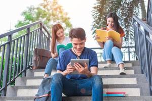 groupe d'étudiants asiatiques lisant et révisant par manuel et ordinateur portable à l'escalier à l'université. concept d'apprentissage de la technologie et de l'éducation. thème de divertissement et ludo-éducatif