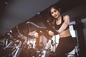 femme asiatique de remise en forme à vélo faisant du filage au gymnase. belle jeune femme travaille sur un vélo de gym. concept médical et sain. thème d'entraînement et cardio photo