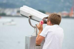 le garçon regards à le observation plate-forme dans une touristique ordinateur de poche télescope. photo