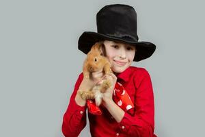 une magicien garçon dans une noir chapeau est en portant une rouge lapin. photo