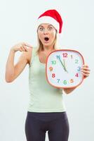 sportif femme avec Père Noël chapeau montrer du doigt à l'horloge photo