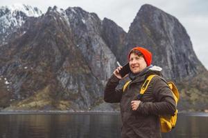 homme parlant au téléphone portable dans un sac à dos jaune debout sur un fond de montagne et d'un lac photo