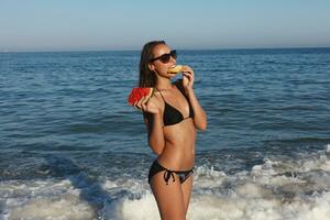 été vacances - Jeune fille en mangeant Frais pastèque sur sablonneux plage photo