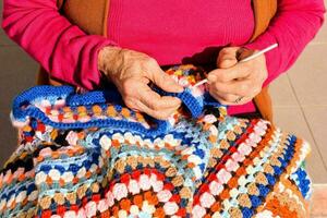 un plus âgée femme est tricot une coloré couverture photo