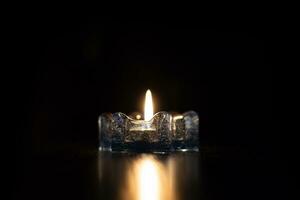 un bougie lumière brûlant vivement dans le noir Contexte dans le la glace chandelier. photo