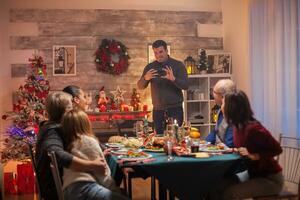 de bonne humeur homme en utilisant téléphone intelligent à prendre Photos de le sien famille à Noël fête.