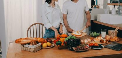 Beau homme séance près le sien épouse à cuisine. famille couple voir social médias, le surf le la toile tandis que séance à cuisine table avec générique portable. couple travail avec portable à Accueil photo