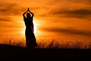 silhouette de une femme jouit méditer à magnifique le coucher du soleil. photo