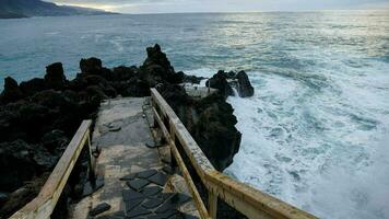 une escalier de premier plan à le océan avec vagues s'écraser contre le rochers photo