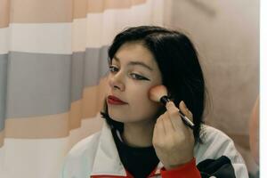 Jeune adolescent femme doucement appliquant maquillage dans de face de miroir avec doux brosse photo