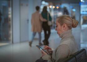 magnifique blond fille dans une chaud chandail dans une grand super marché sur une banc photo