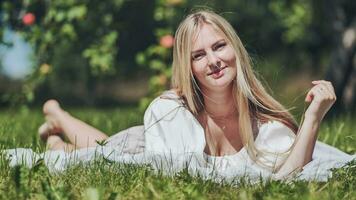 une blond fille mensonges dans une clairière dans un Pomme verger. photo