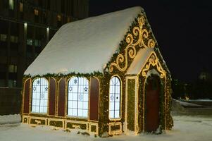 Nouveau années, Noël pain d'épice décoratif enfants loger, décoré avec lumineux motifs et guirlandes. de fête hiver ville éclairage. photo