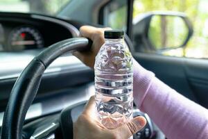 chauffeur de femme asiatique tenant une bouteille pour boire de l'eau en conduisant une voiture. une bouillotte en plastique provoque un incendie. photo